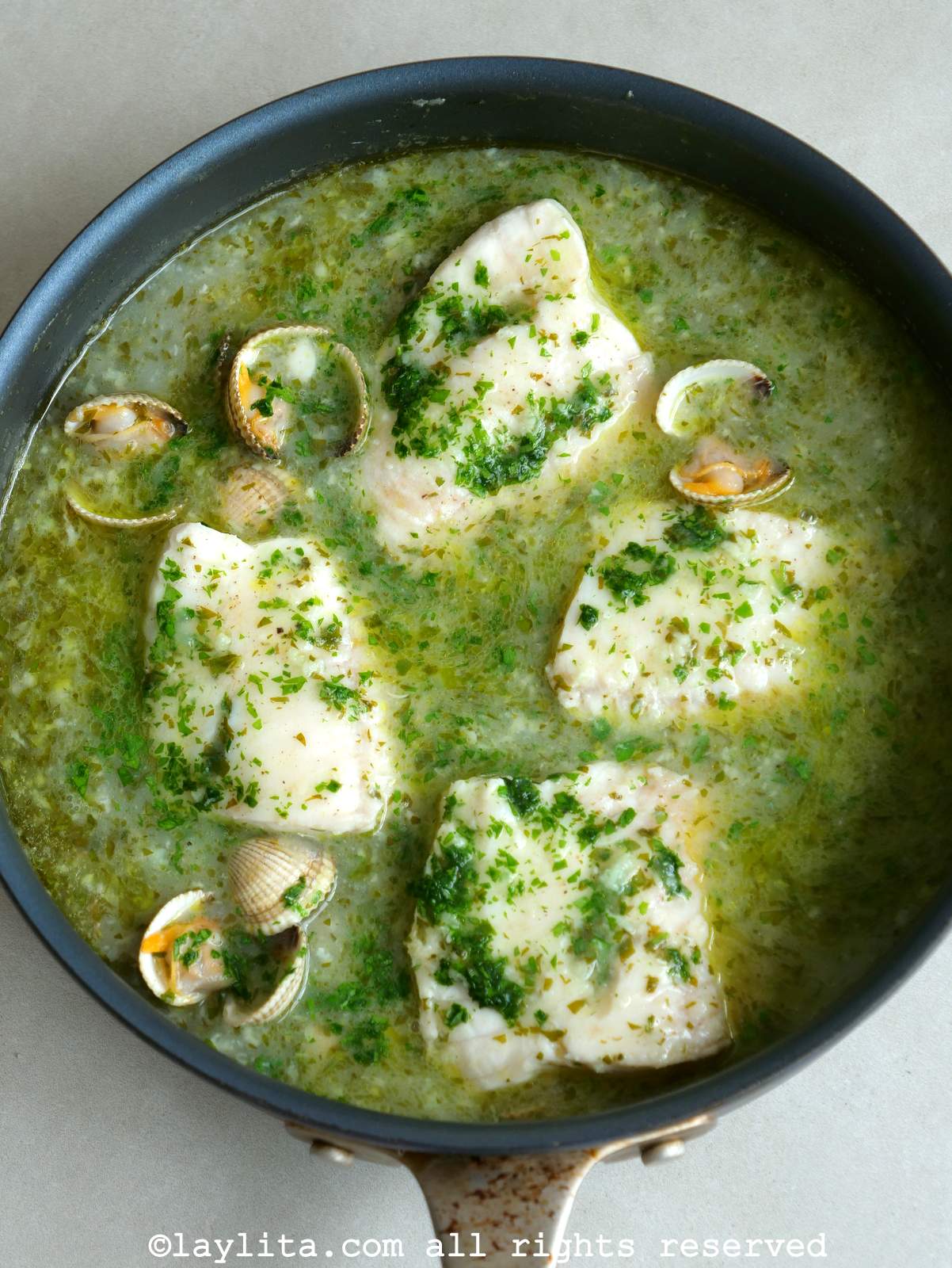Vista desde arriba de pescado en salsa verde con almejas servido en una sartén
