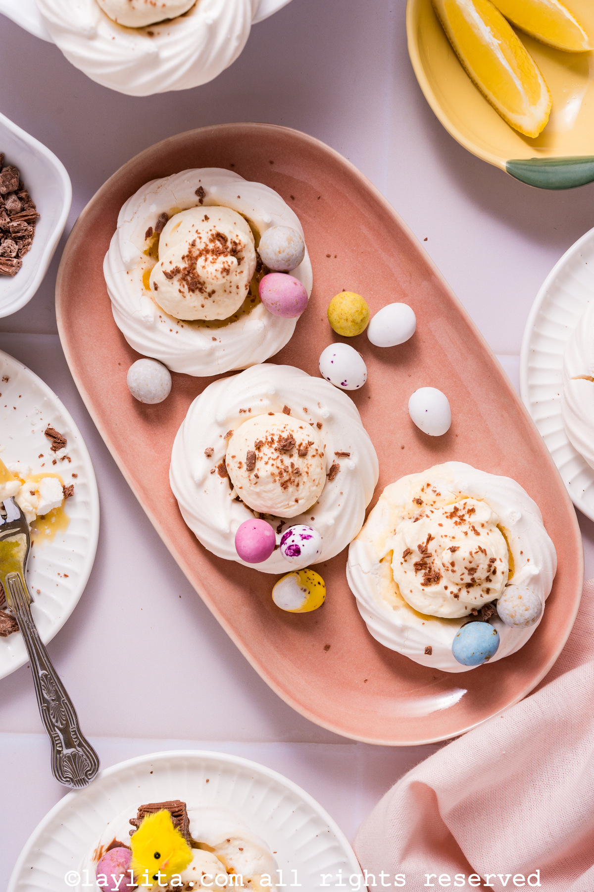 Vista superior de  una bandeja con tres mini pavlovas o nidos de merengue rellenos para Pascua con decoraciones de Pascua alrededor