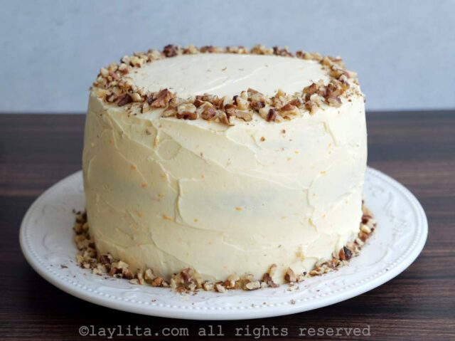 Un pastel decorado con cobertura de queso crema y nueces trituradas