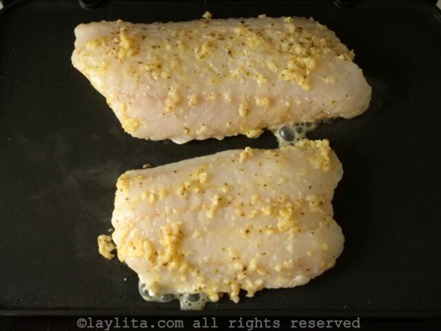 Dos filetes de pescado cocinandose en una plancha