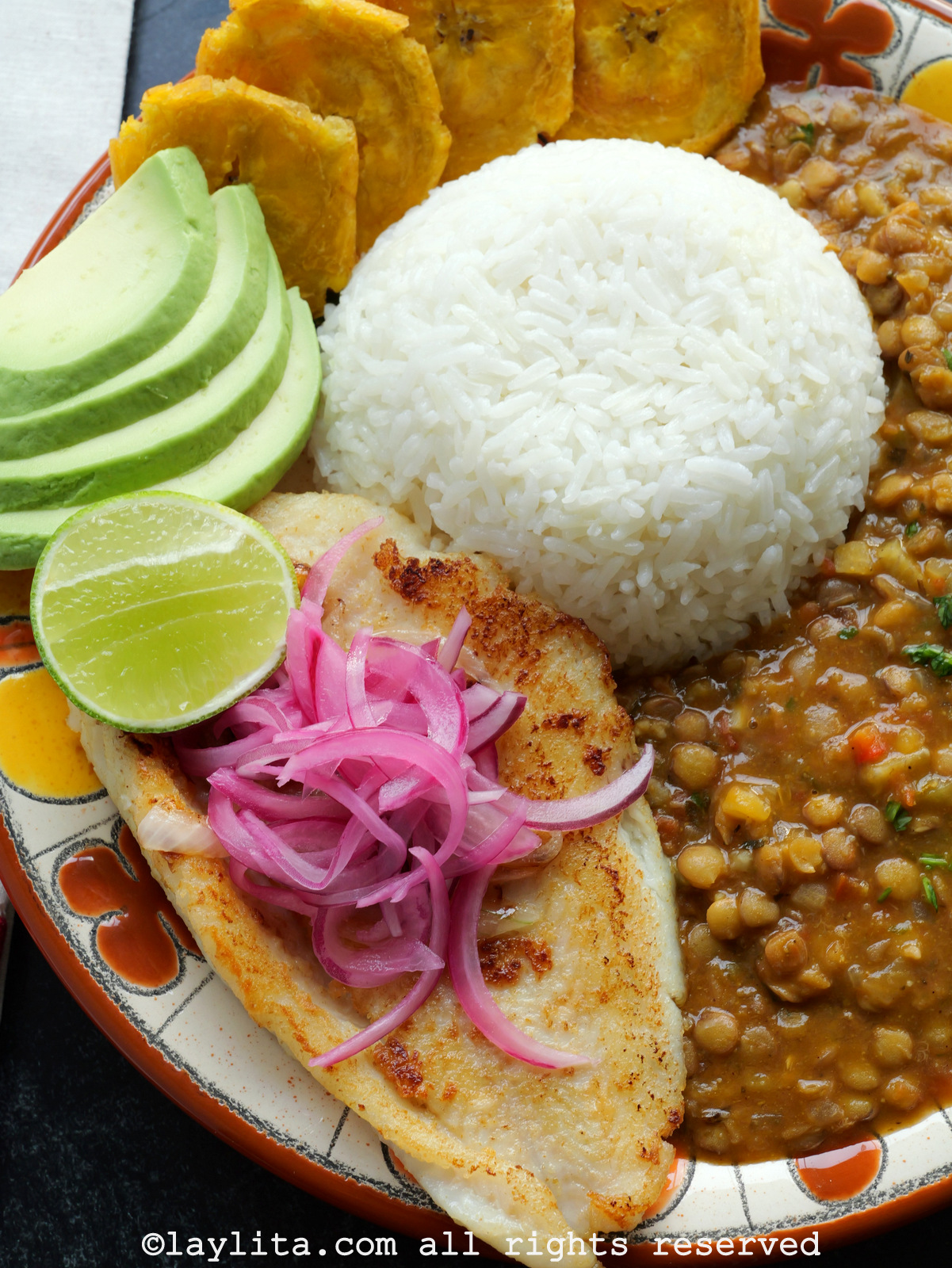 Primer plano de un filete de pescado a la plancha servido en un plato con arroz y lentejas, con cebolla roja encima.