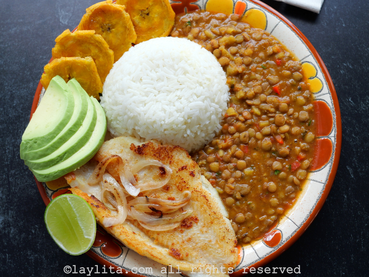 Pescado a la plancha en un plato acompañado de arroz, plátanos y lentejas.