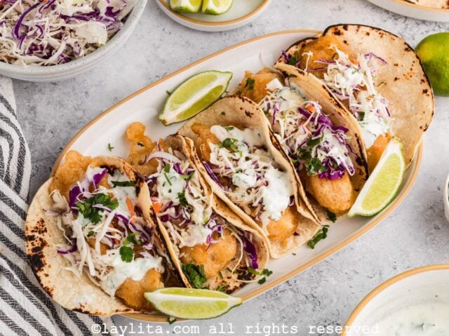 Cinco tacos de pescado en una fuente con rodajas de limón alrededor