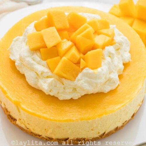 Cheese de Mango decorado con crema chantilly y trozos de mango fresco en un plato blanco