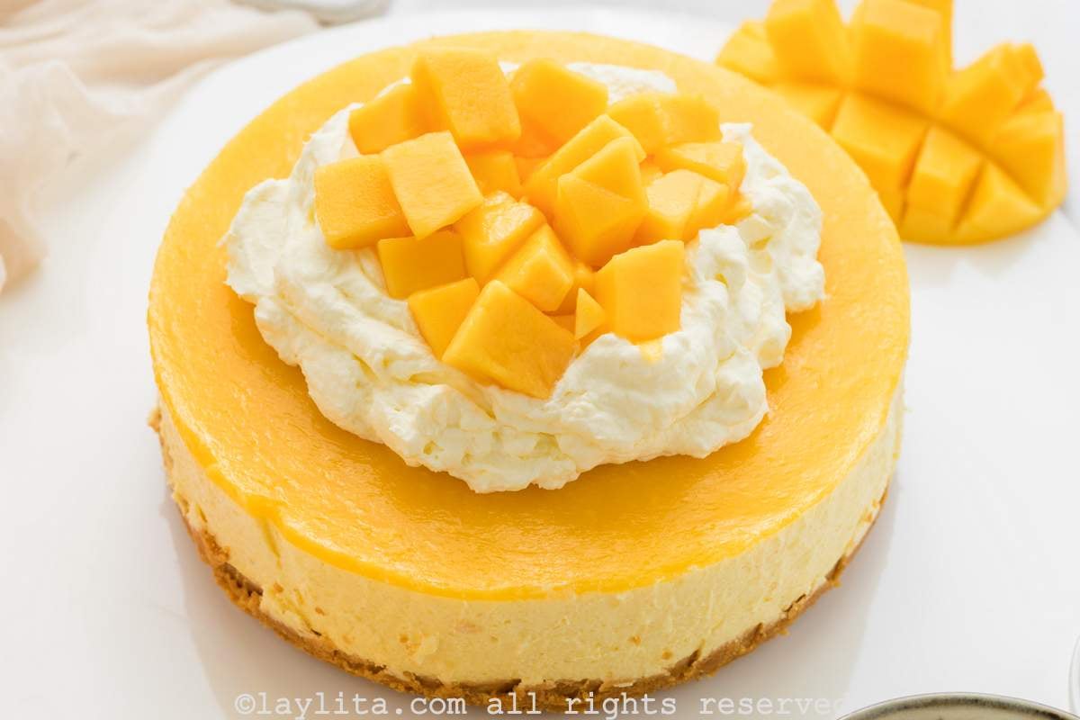 Cheese de Mango decorado con crema chantilly y trozos de mango fresco en un plato blanco