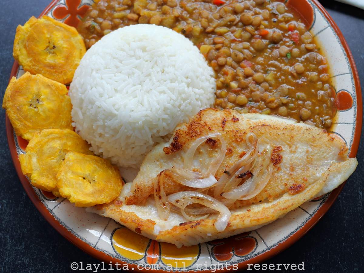 Pescado a la plancha en un plato acompañado de arroz, plátanos y lentejas.