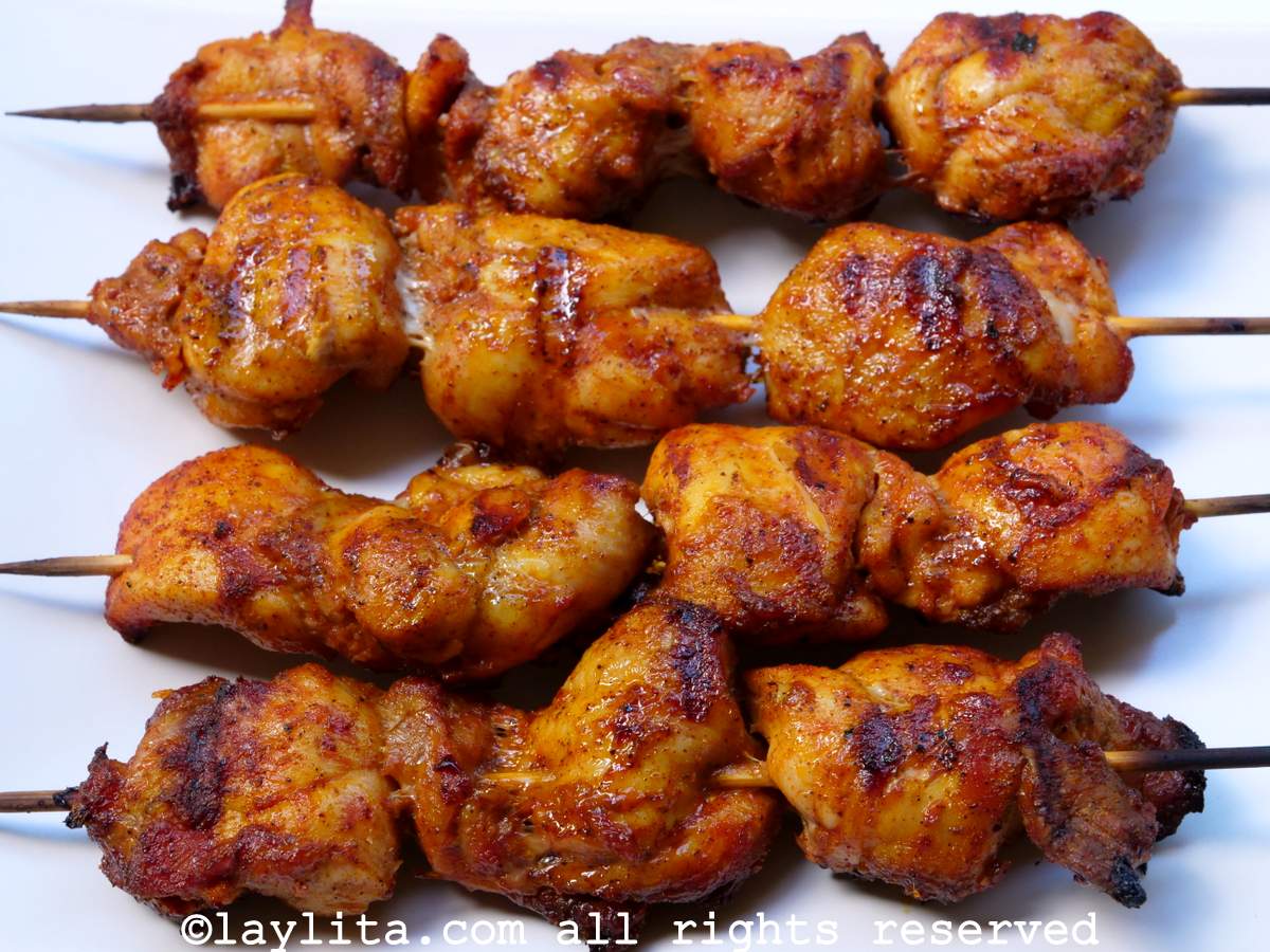 Primer plano de cuatro brochetas de pollo en un plato blanco