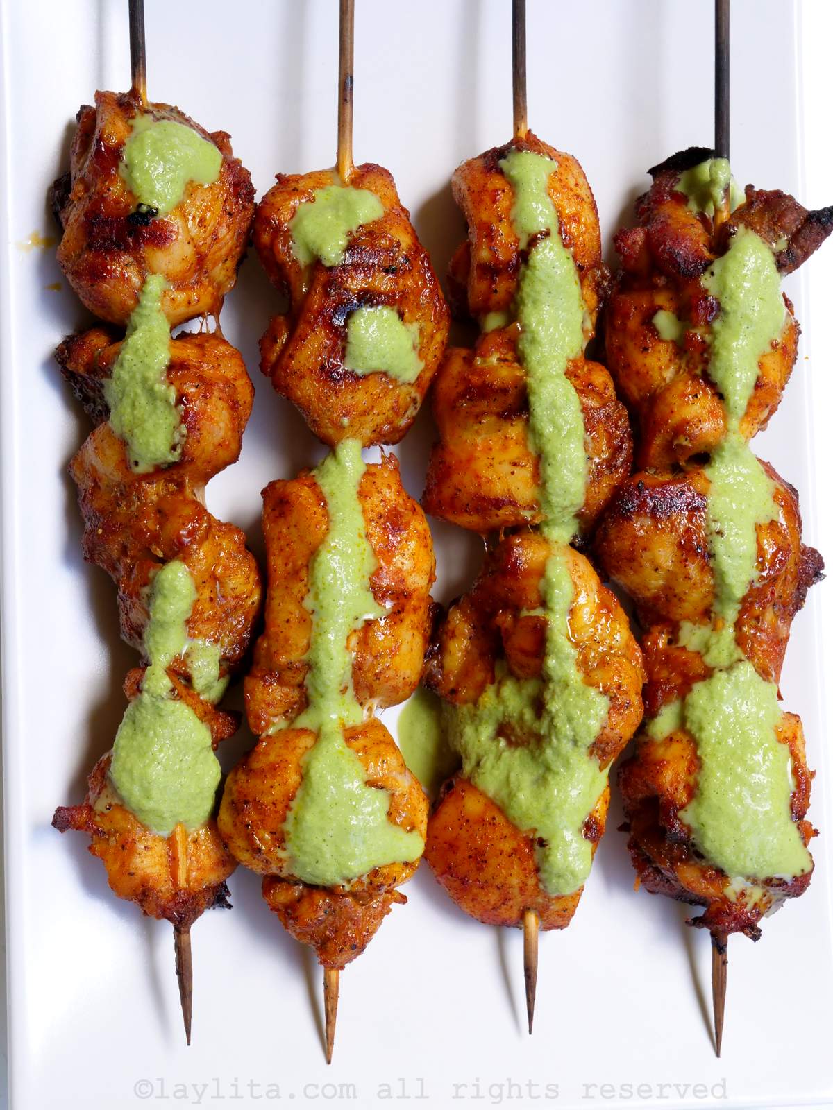 Cuatro brochetas o pinchos de pollo con una salsa verde encima