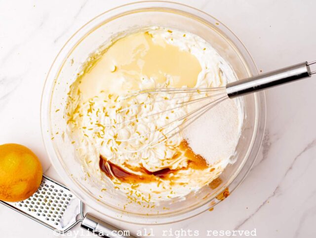 Ralladura de naranja, la leche condensada, la vainilla y el azúcar siendro agregadas al bol con el queso crema batido