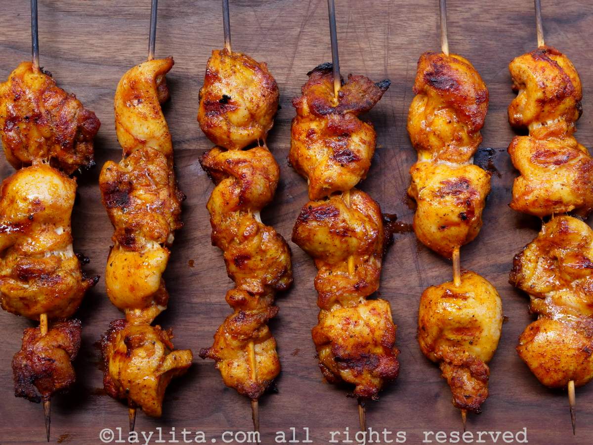 Varios pinchos de pollo asados encima de una tabla de madera
