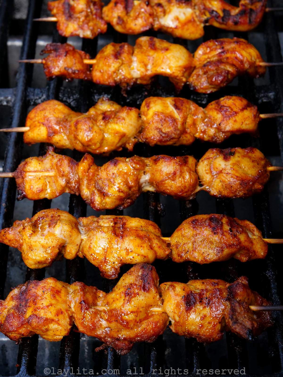 Vista superior de varios pinchos de pollo asándose a la parrilla