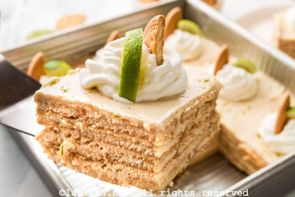 Una espátula con una porción de carlota de limón, con el resto del postre en la bandeja de servir 