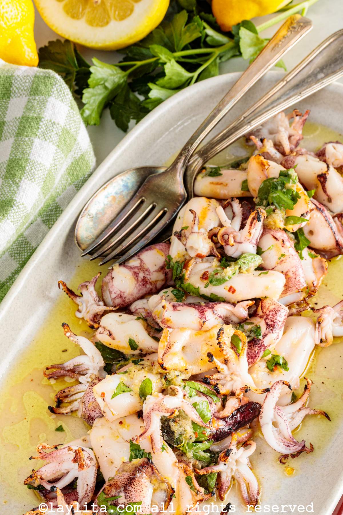 Primer plano de una ensalada de calamares asados con hierbas picadas encima y rodajas de limón al lado