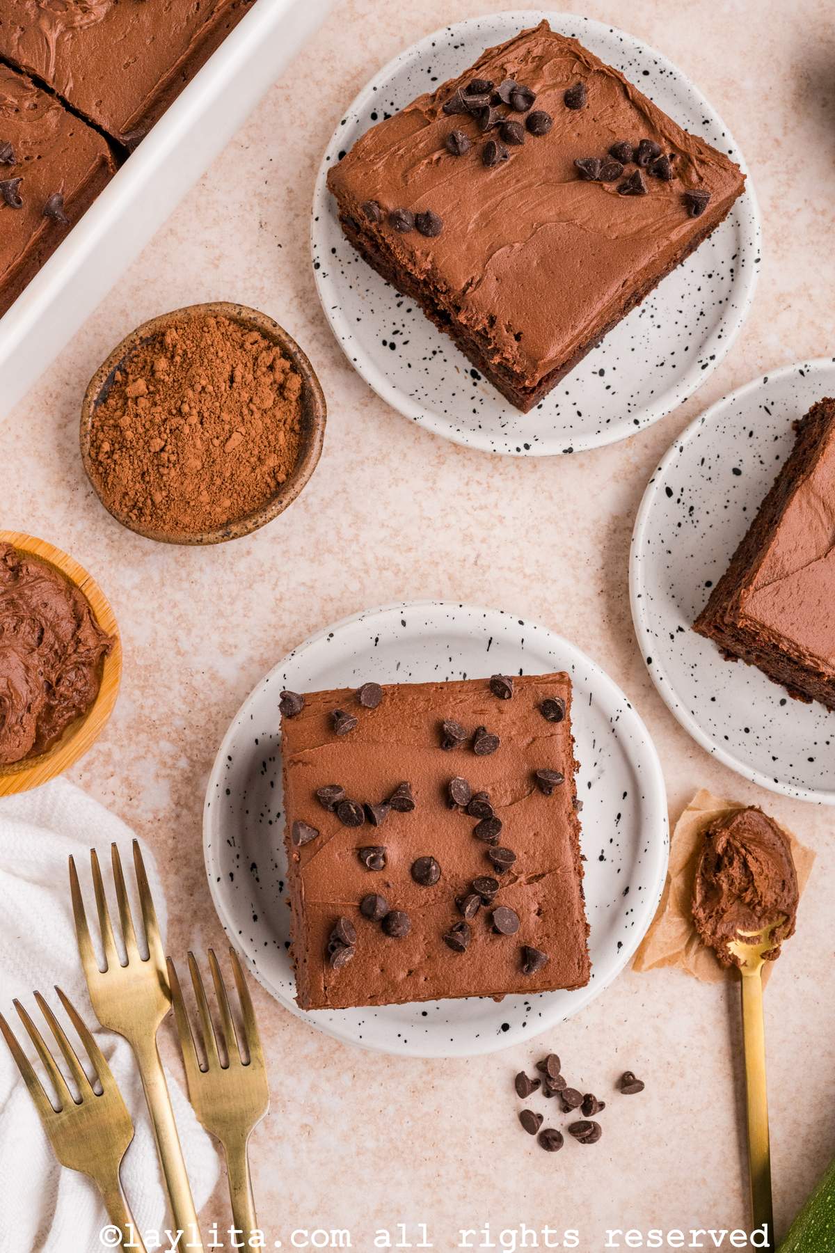 Vista lateral de varias rebanadas de torta de chocolate y calabacín con tenederos y una cuchara con betún de chocolate al lado