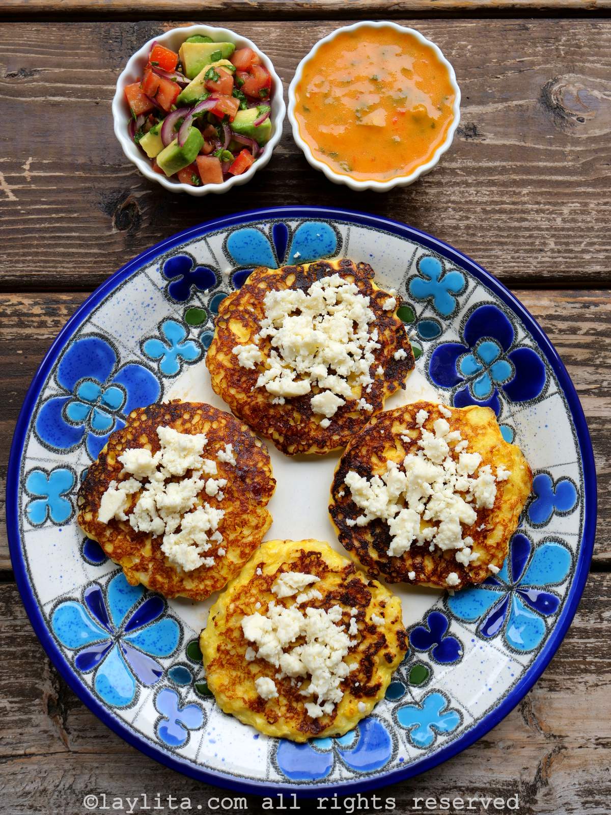 Vista superior de un plato con cuatro torrejas de maíz tierno con queso encima, en la parte lateral hay dos bols con salsas