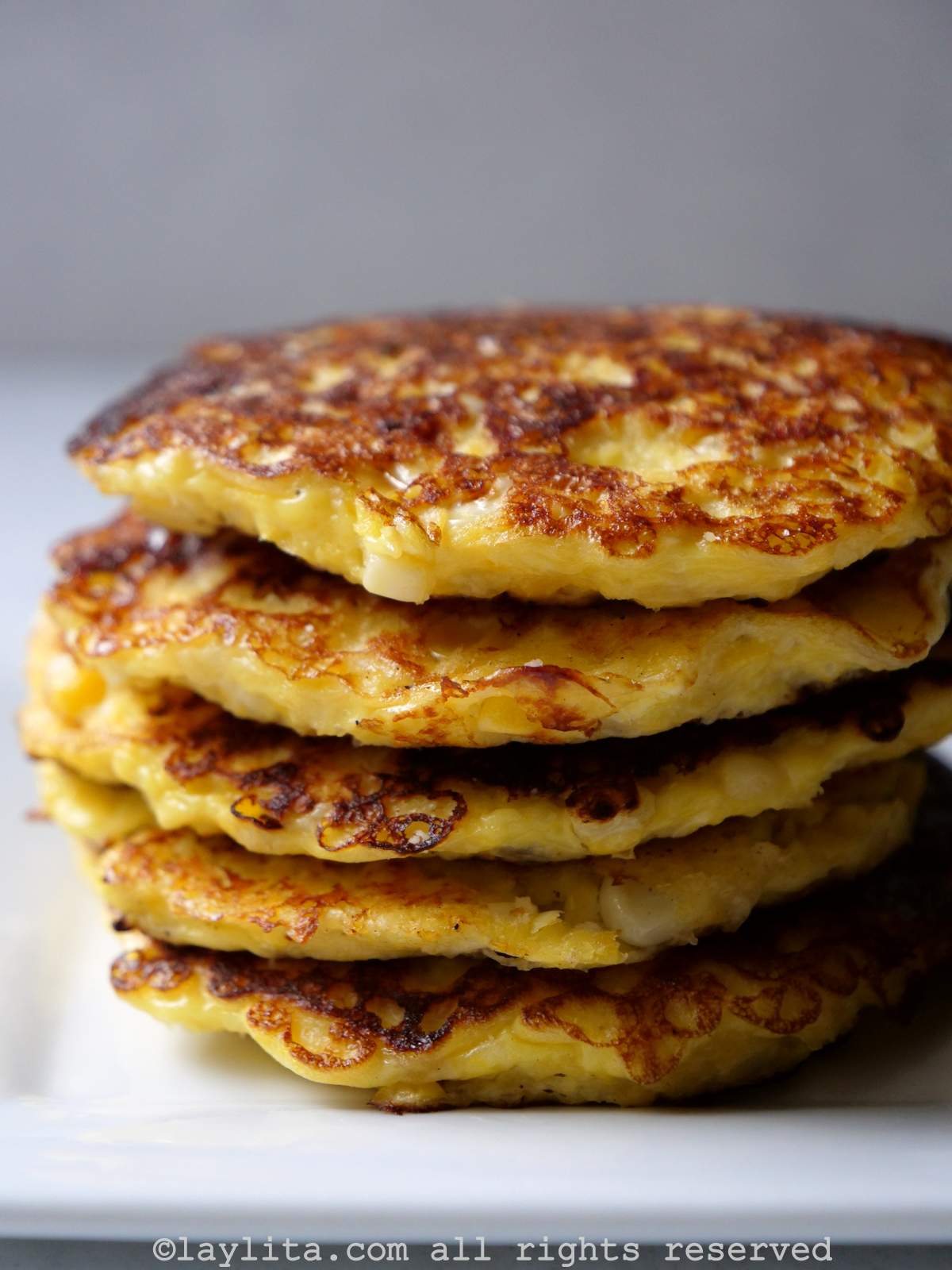 Vista lateral de cinco tortitas o panqueques de maíz y queso apiladas una sobre otra en un plato blanco