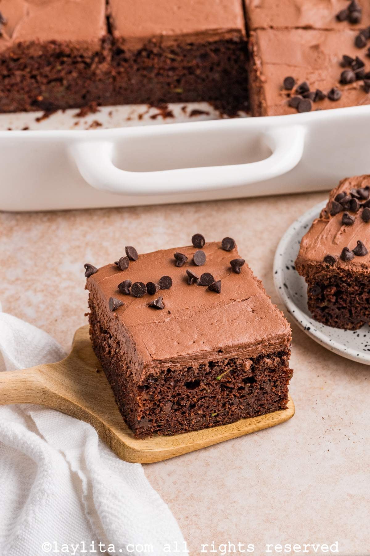 Una rebanada de torta de chocolate en una espátula con el resto del pastel en el fondo