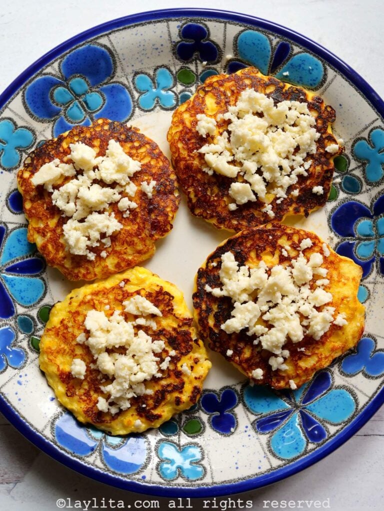 Cuatro torrejas de maíz con queso encima en un plato con flores azuladas