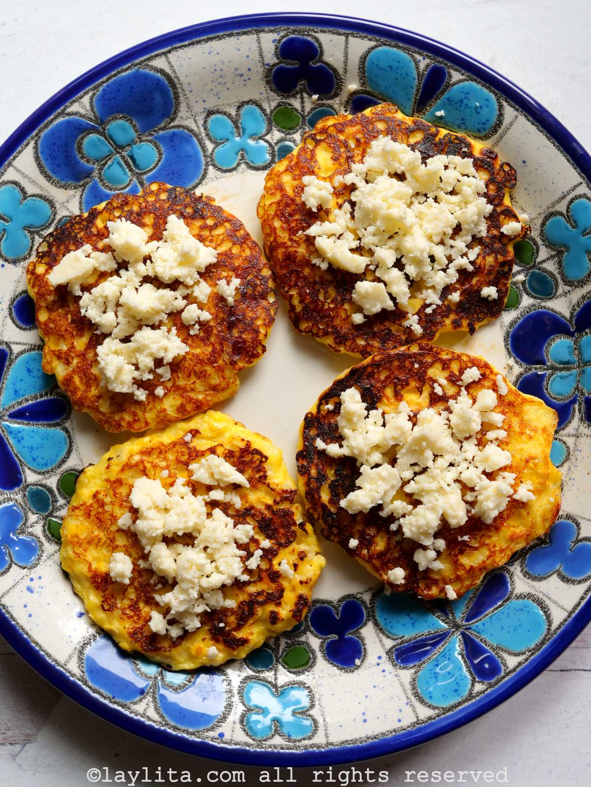 Cuatro torrejas de maíz con queso encima en un plato con flores azuladas