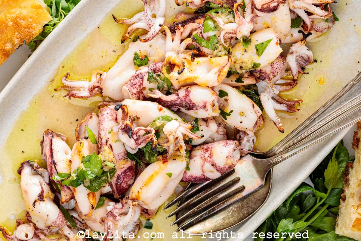Vista superior de un plato blanco con ensalada de calamar asado con utensilios para servir al lado
