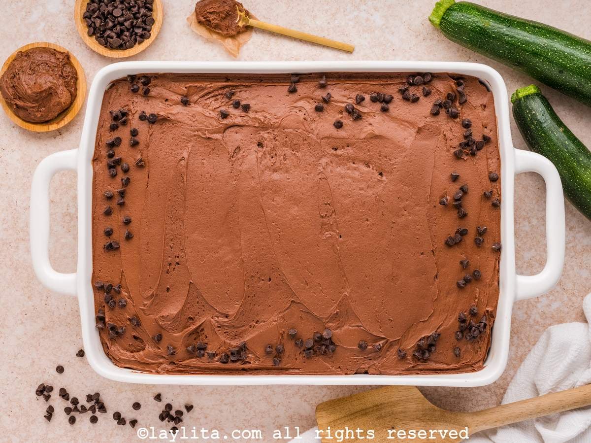 Vista superior de un pastel de chocolate en un molde blanco con chispas de chocolate encima y zucchinis al lado