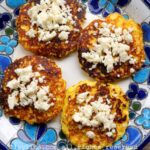 Cuatro torrejas de maíz con queso encima en un plato con flores azuladas encima de una mesa de madera