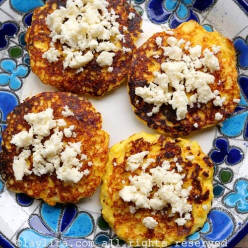 Cuatro torrejas de maíz con queso encima en un plato con flores azuladas encima de una mesa de madera