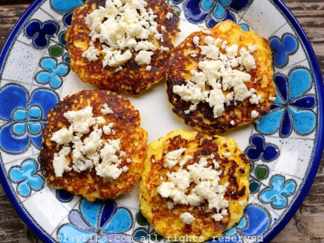 Cuatro torrejas de maíz con queso encima en un plato con flores azuladas encima de una mesa de madera
