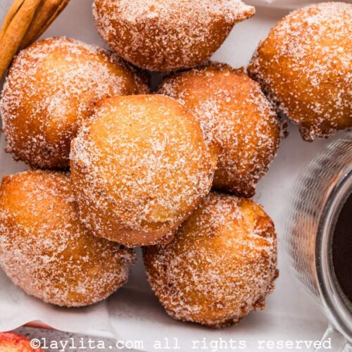 Vista superior de varios buñuelos dulces con azúcar encima y una salsa dulce en el fondo