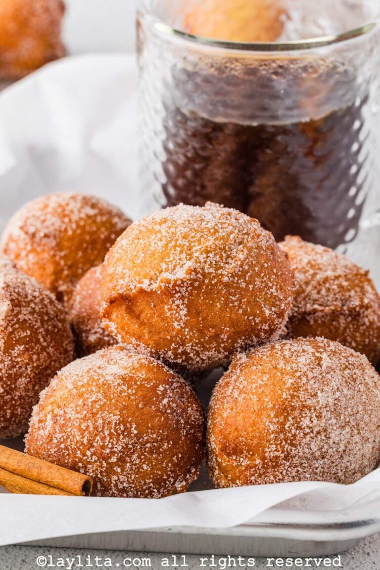 Primer plano de varios buñuelos dulces con azúcar encima y una salsa dulce en el fondo
