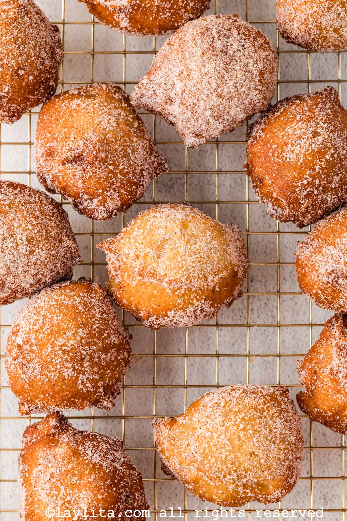 Primer plano de varios buñuelos espolvoreados con azúcar y canela encima de una rejilla de hornear