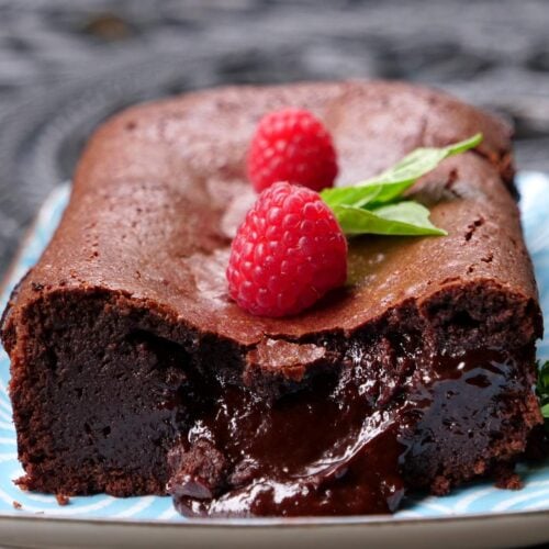 Gâteau au chocolat fondant garni de framboises, présenté sur un plat bleu.