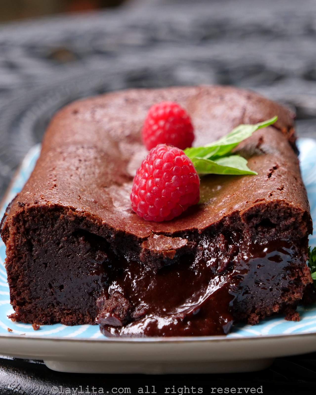 Gâteau au chocolat fondant garni de framboises, présenté sur un plat bleu.