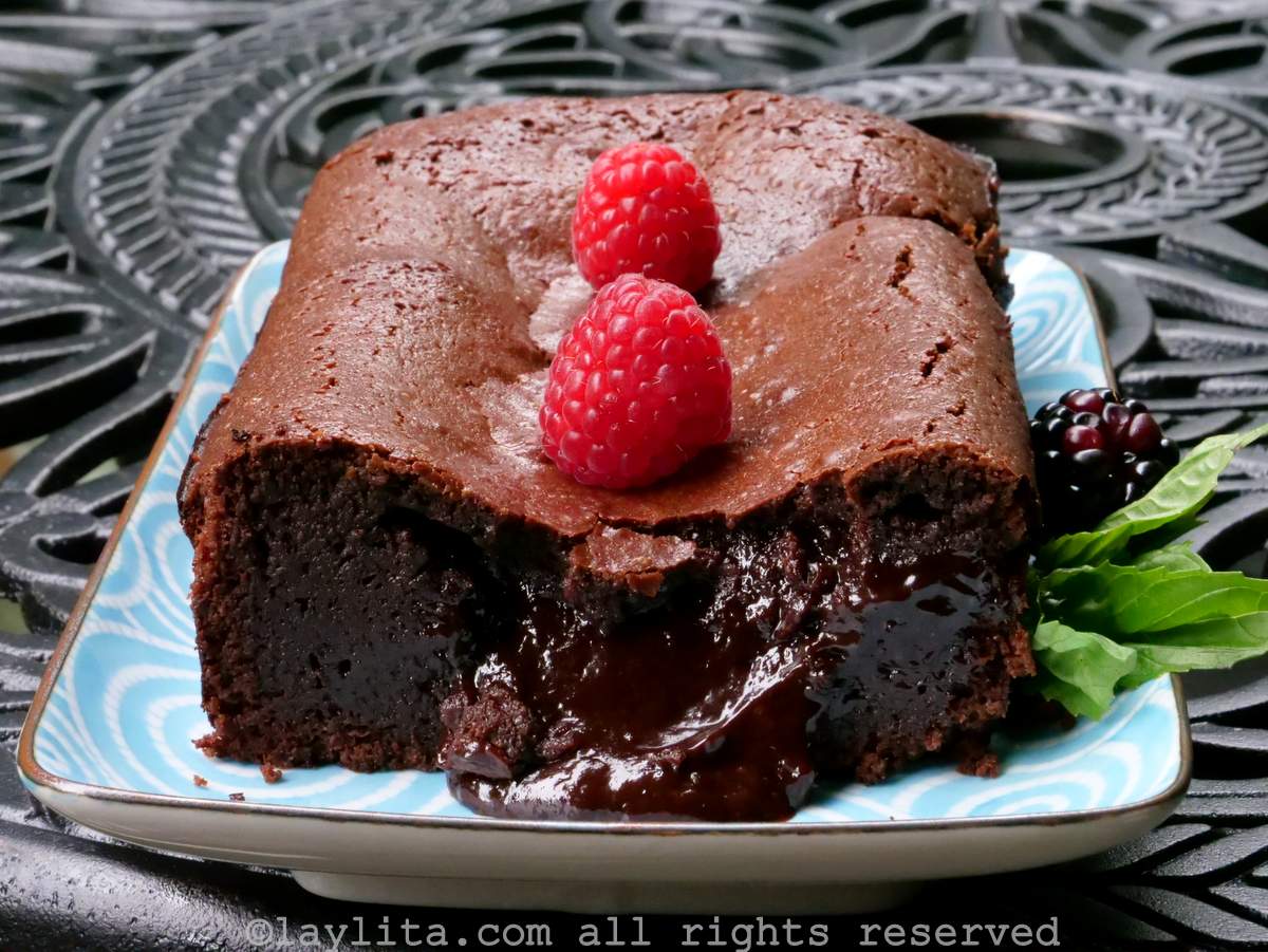 Gâteau moelleux fondant au chocolat garni de framboises et de feuilles de basilic, présenté sur un plat bleu.