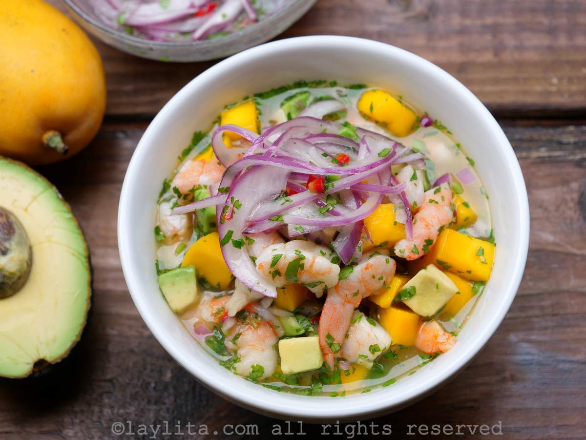 Un bol blanc de ceviche de crevettes à la mangue et à l'avocat, garni d'oignons rouges marinés.