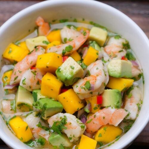 Un bol blanc rempli de ceviche de crevettes à la mangue et à l'avocat sur une table en bois