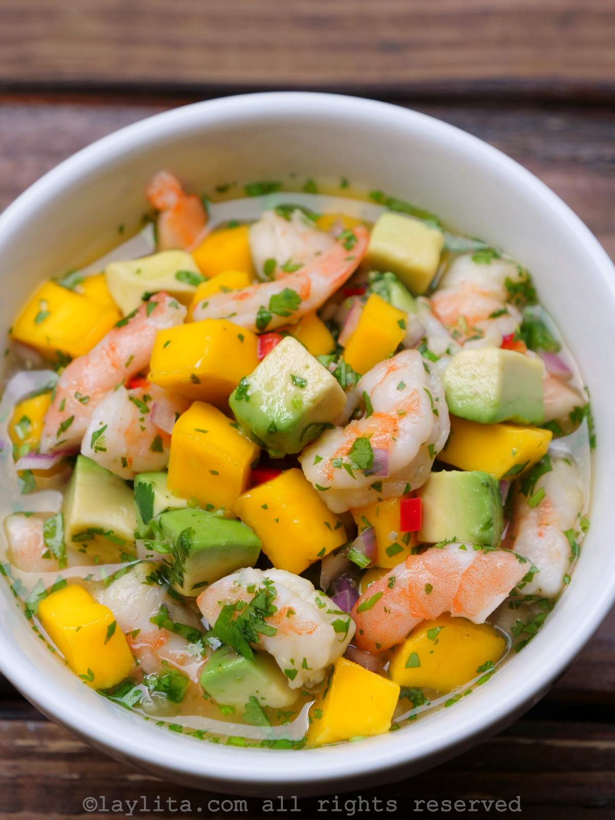 Un bol blanc rempli de ceviche de crevettes à la mangue et à l'avocat sur une table en bois