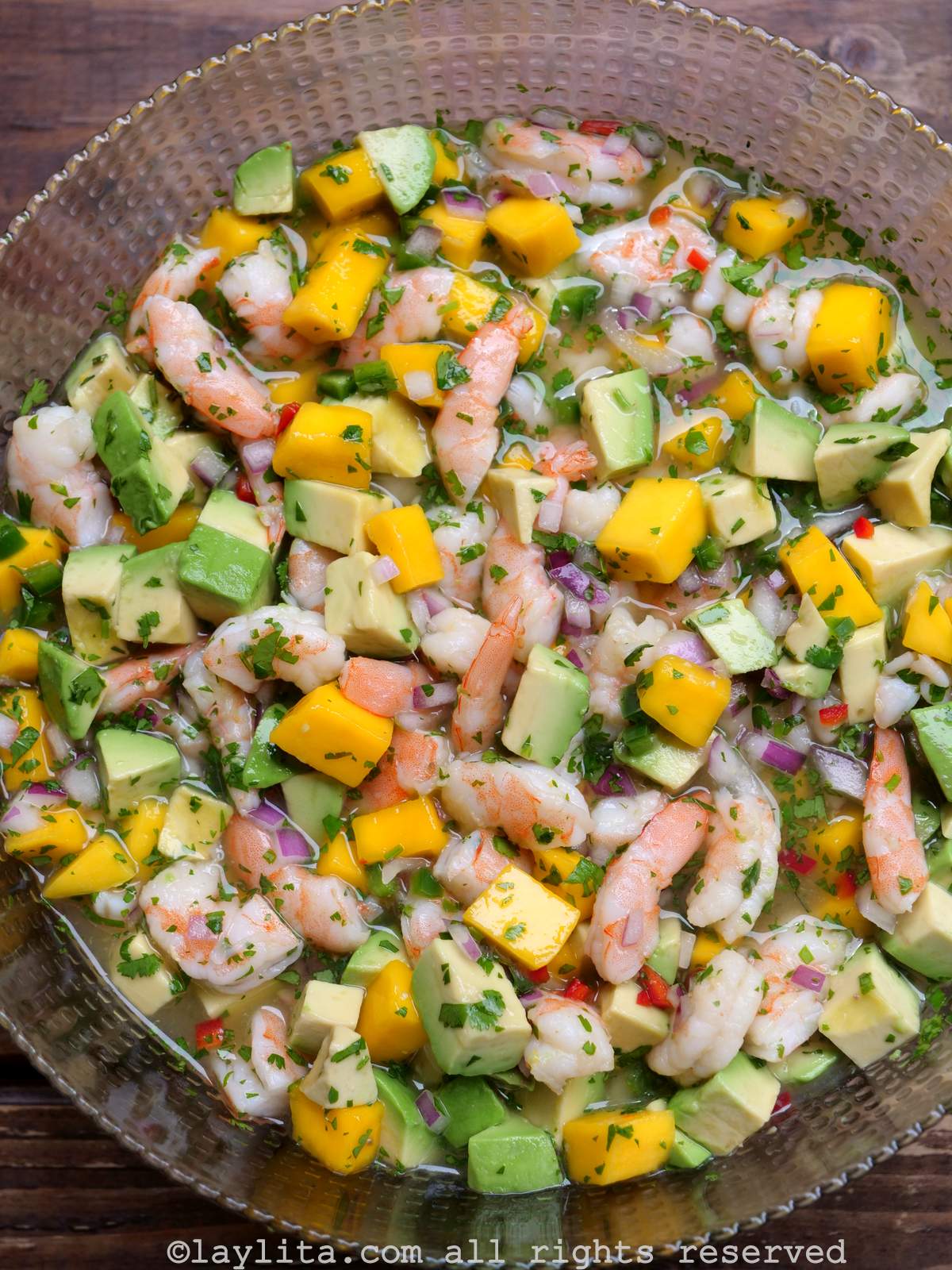 Ceviche de crevettes à la mangue et à l'avocat, servi dans un bol en verre sur une table en bois.