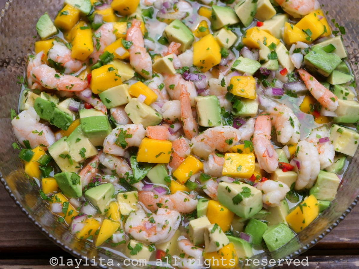 Ceviche de crevettes à la mangue et à l'avocat, servi dans un bol en verre sur une table en bois.