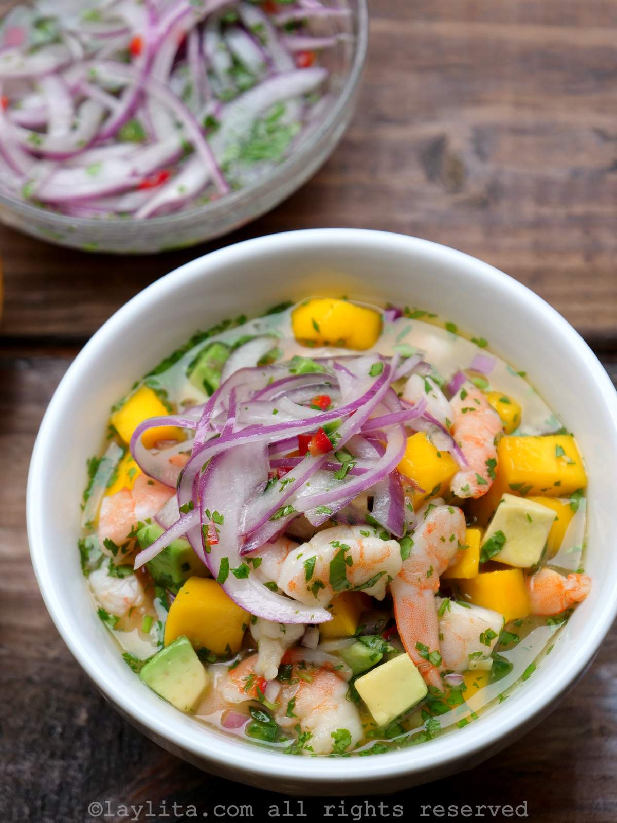 Un bol blanc de ceviche de crevettes à la mangue et à l'avocat, garni d'oignons rouges marinés.