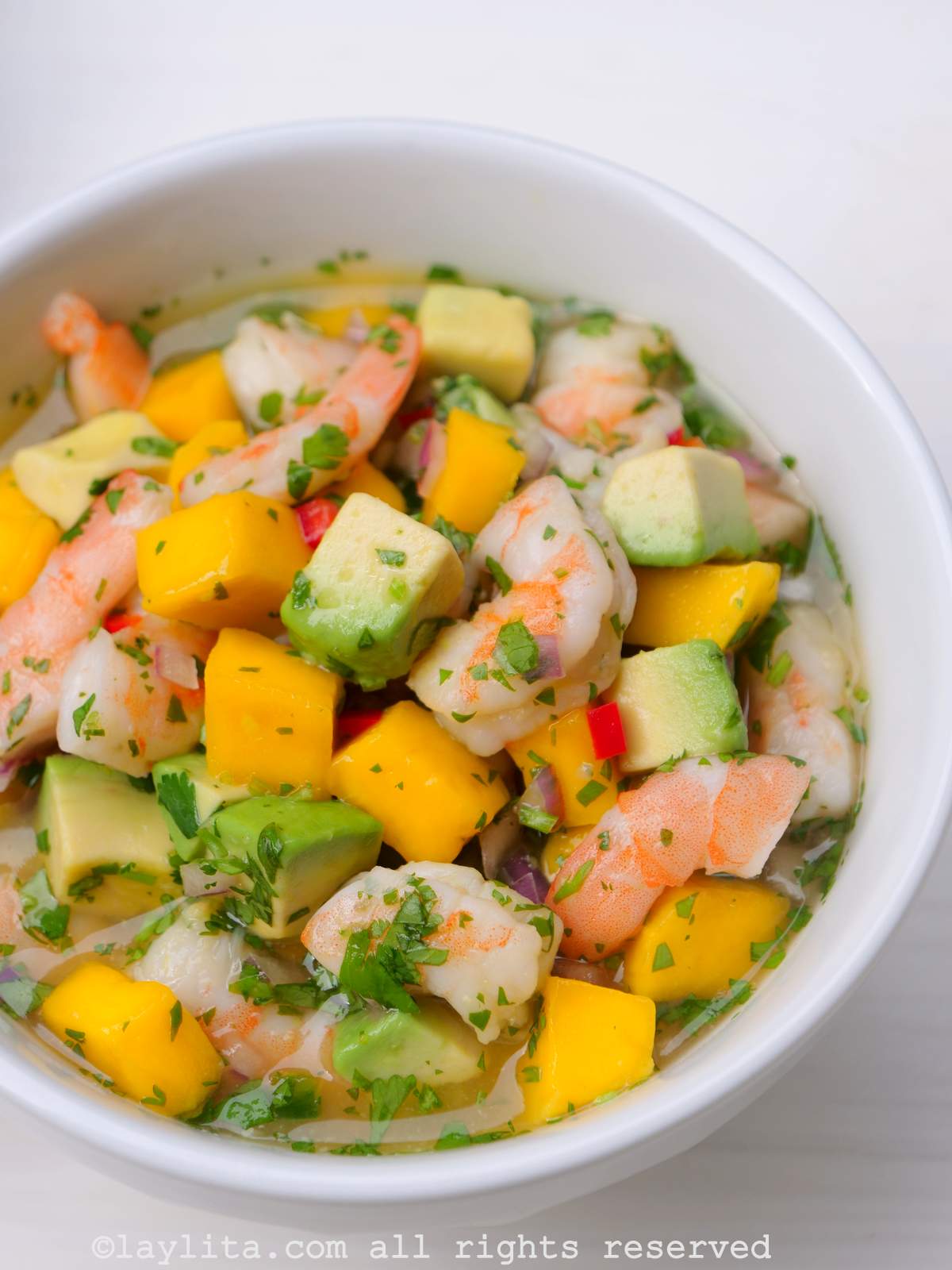 Un bol blanc rempli de ceviche de crevettes à la mangue et à l'avocat sur une table blanche