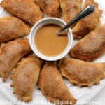 Empanadas aux pommes et à la cannelle sur une assiette blanche, servies avec une sauce caramel au dulce de leche