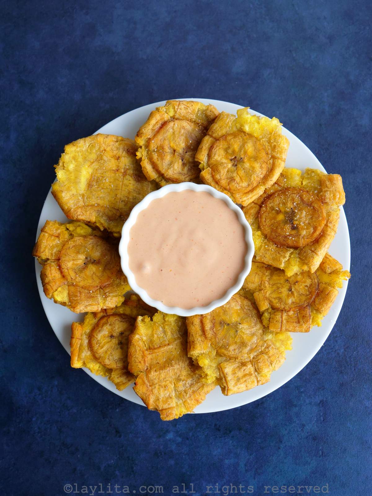 Plate of patacones or tostones plantain chips with salsa rosada on a white plate