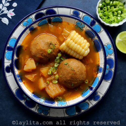 A floral soup bowl full of Ecuadorian green plantain ball soup with a lime half and diced green onions on the side