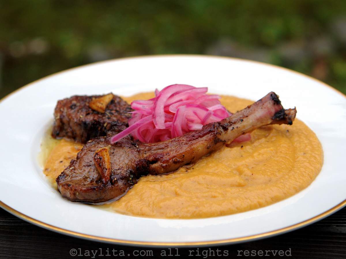 A white plate with ripe plantain purée, lamb chops and pickled red onions