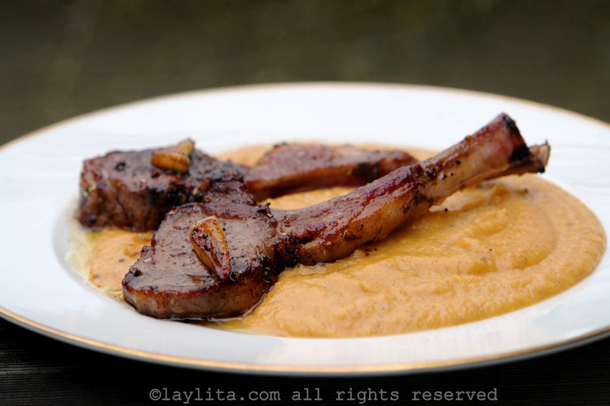 Ripe plantain purée with lamb chops on top on white plate with a gold rim