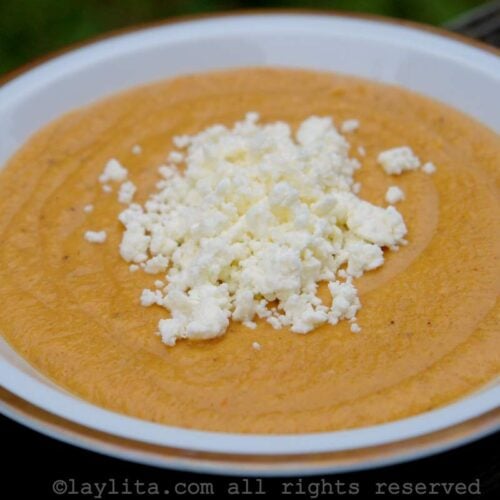 A white bowl with ripe plantain purée topped with crumbled cheese