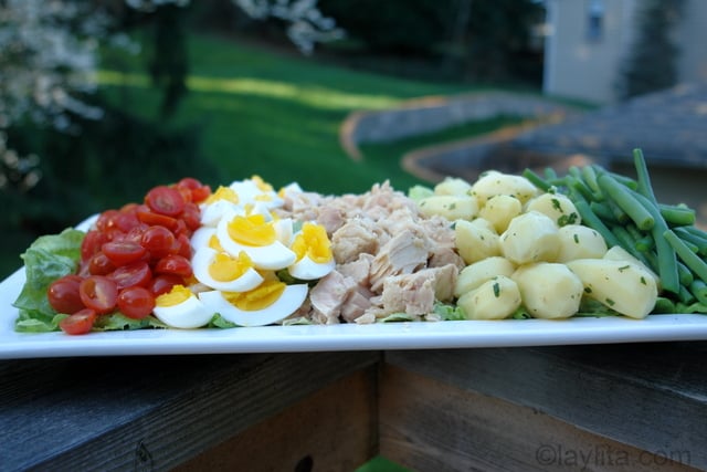 Une partie des ingrédients de cette salade niçoise inclue des petites tomates, des œufs, du thon, des petites pommes de terre, et des haricots verts.