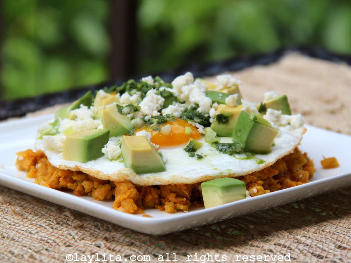 A white square plate with Ecuadorian majado de verde or mashed plantains with fried egg, cheese, avocado and aji sauce