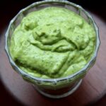 Overhead shot of avocado sauce in a glass bowl on a wood background